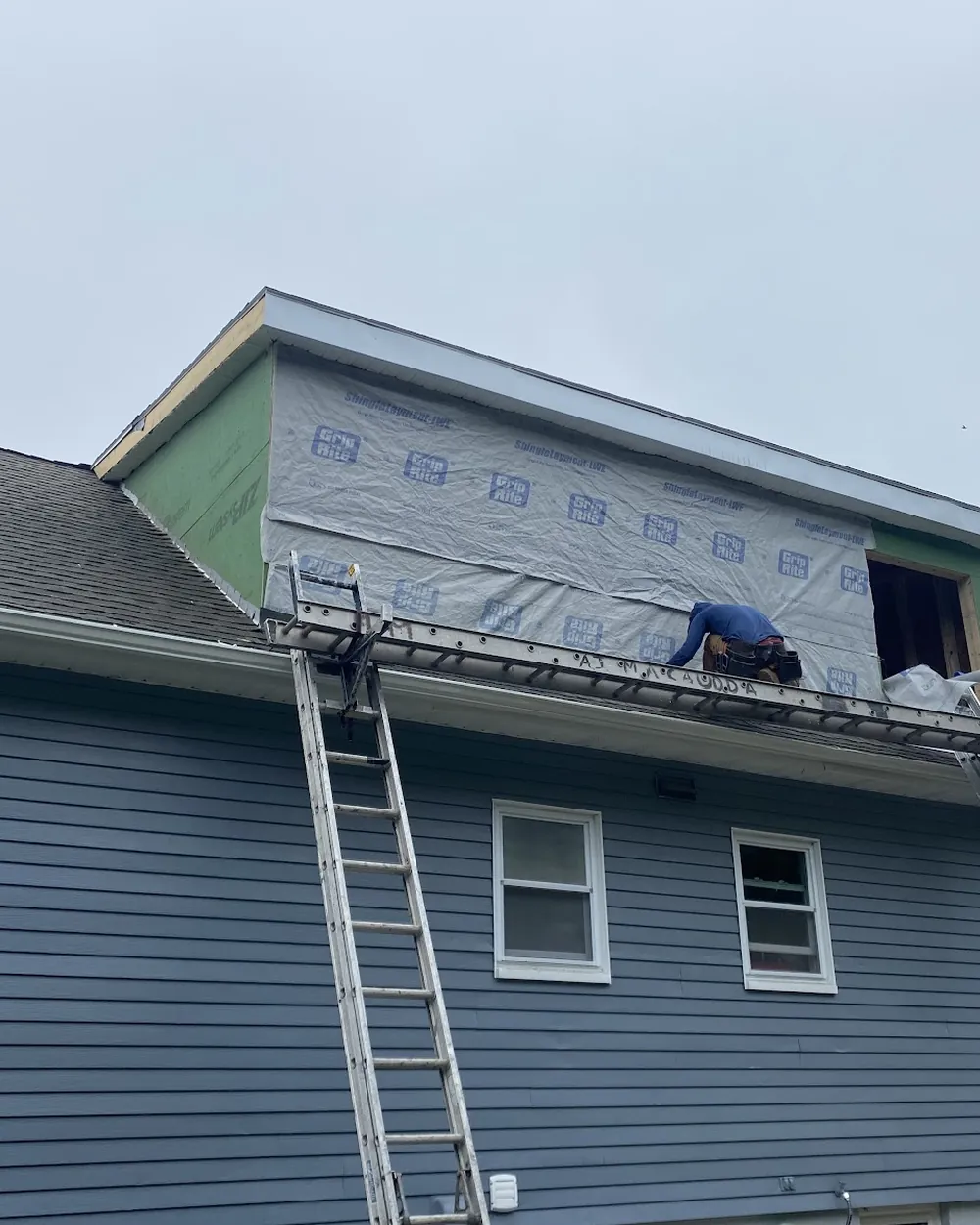 Exterior work in progress on a house, ladders against new siding